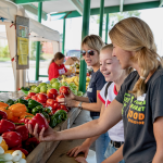 Farmers Market Food Navigator at a farmers market showing a red pepper to a teen girl and her mom