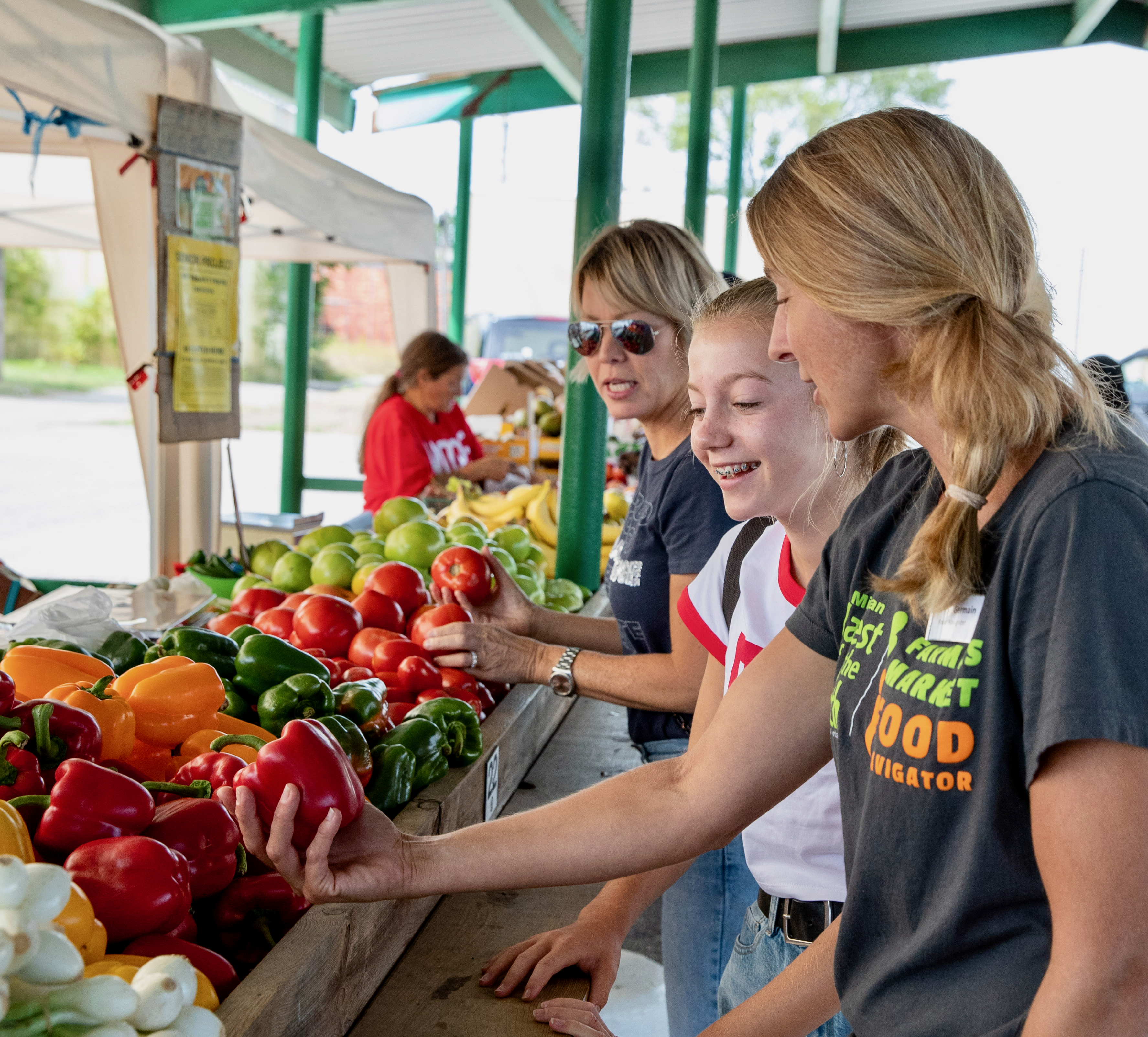 Farmers Market Food Navigator at a farmers market showing a red pepper to a teen girl and her mom